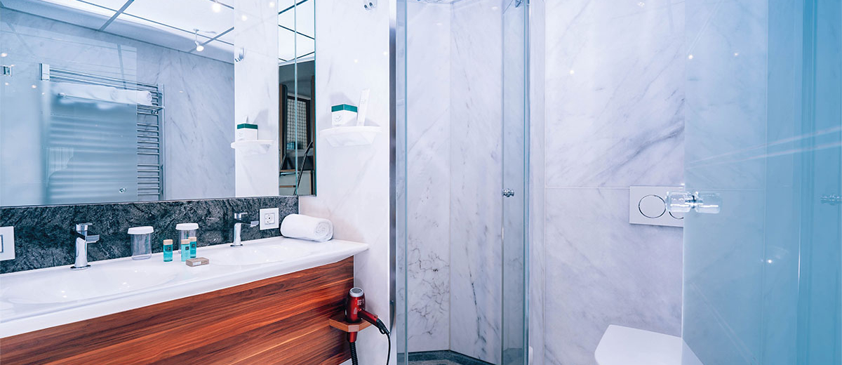 Hotel Victory Therme Erding Bellezza Modern und hell ausgestattetes Badezimmer mit Toilette, Waschbecken und Dusche