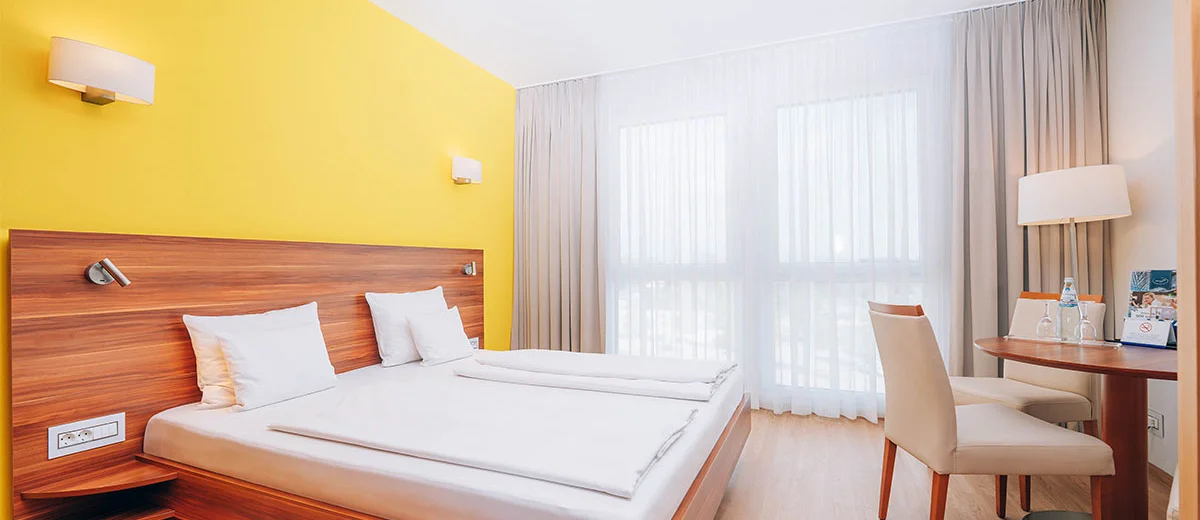 Hotel Victory Therme Erding Bellezza Helles familienfreundliches Hotelzimmer mit Dopplbett, Tisch und Stühlen